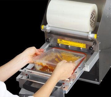 Mani che chiudono una confezione con l'apposita macchina  saldatrice con film